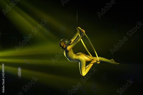 Flexible young woman make performance on aerial hoop, flexible back on aerial hoop, aerial circus show, yellow light. 