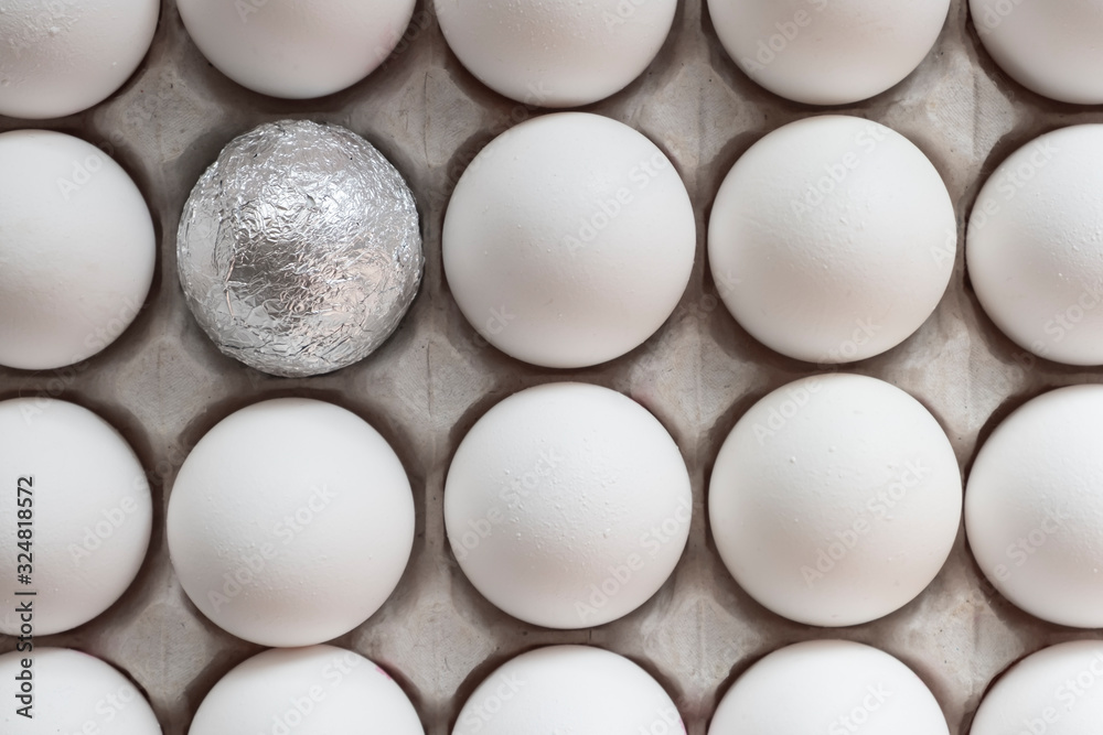 White chicken eggs in a cardboard box with one egg wrapped in foil, background. White chicken eggs in a cardboard box with one egg wrapped in foil, background.