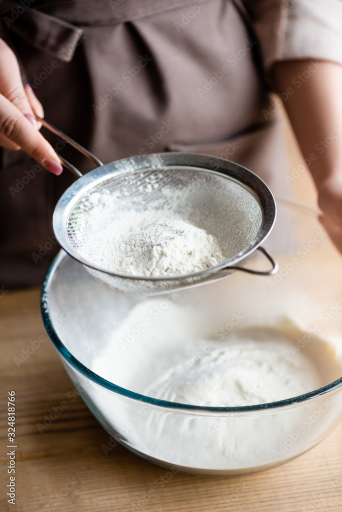 cropped view of young woman sieving flour in glass bowl cropped view of young woman sieving flour in glass bowl