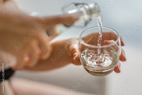 Pouring water from a bottle into a glass on blurred background. Water, Earth, ecology concept