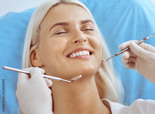 Smiling blonde woman examined by dentist at dental clinic. Healthy teeth and medicine concept