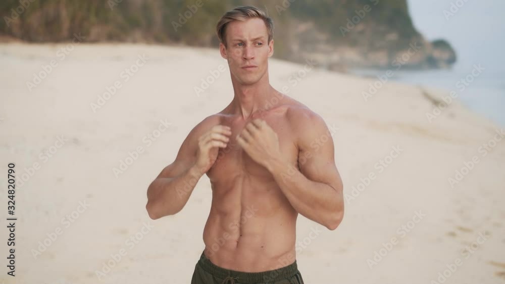 man poses for camera showing muscular body on sand beach