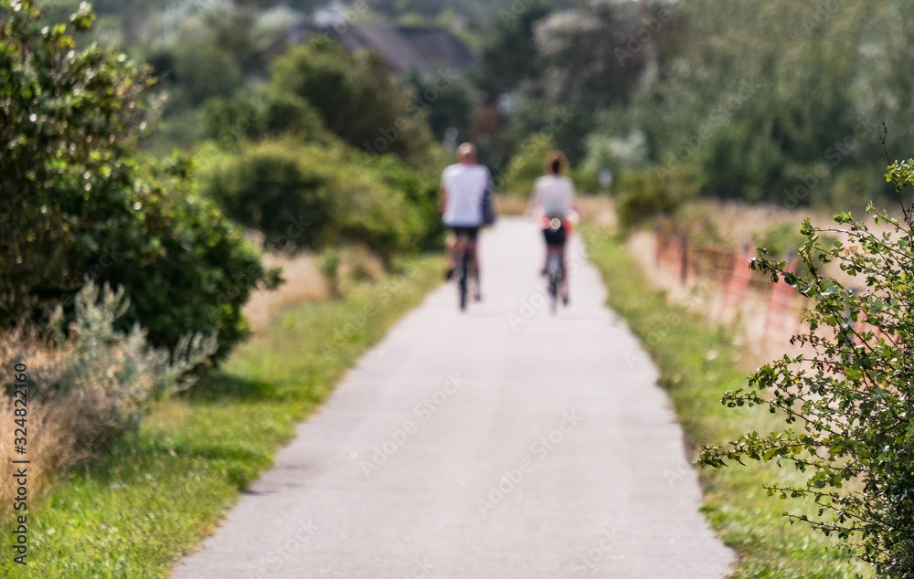 Kein Fokus, bewusst unscharf: Junges Paar fährt im Sommer mit Fahrrädern durch eine nordische Naturlandschaft, grafisches Element, extra ohne Fokus