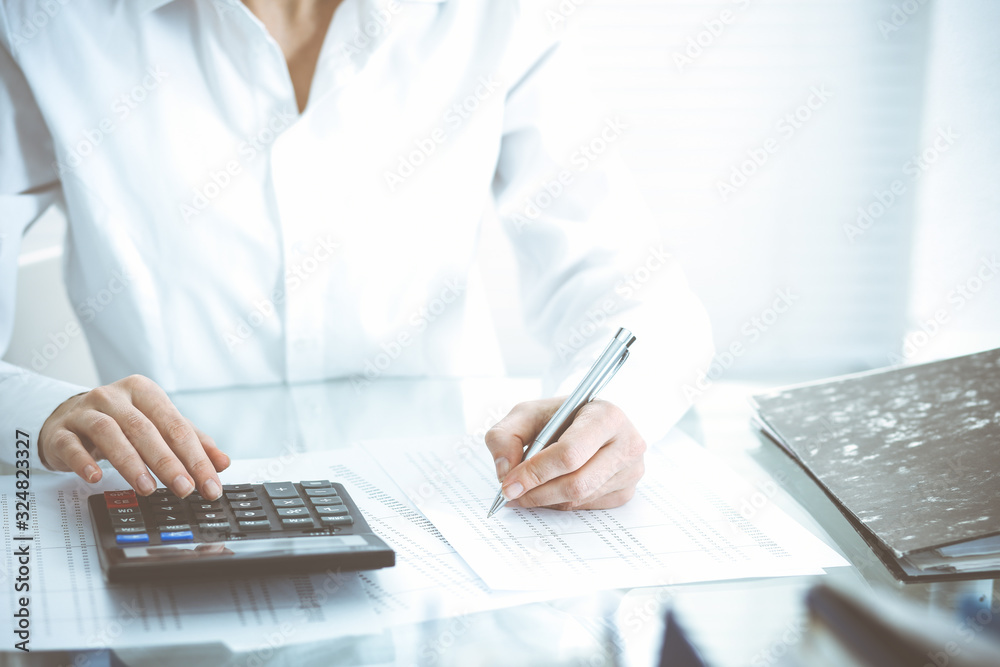 Bookkeeper woman or financial inspector making report, calculating or checking balance, close-up. Business, audit or tax concepts Bookkeeper woman or financial inspector making report, calculating or checking balance, close-up. Business, audit or tax concepts