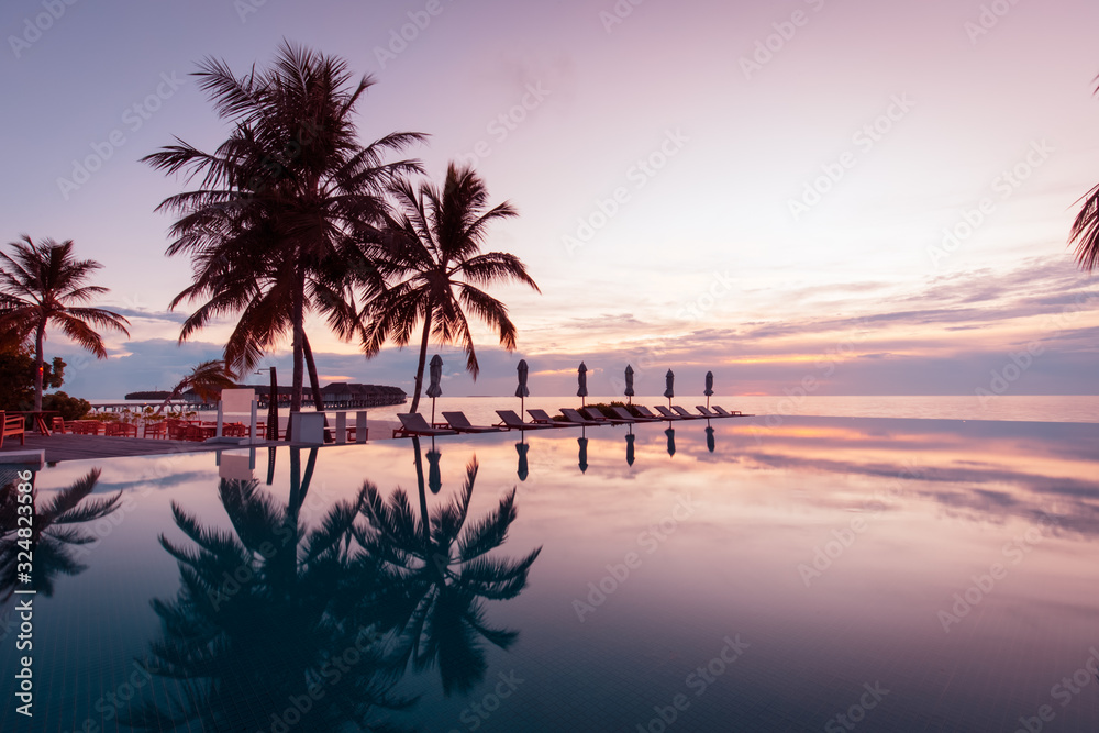 Beautiful poolside and sunset sky. Luxurious tropical beach landscape, deck chairs and loungers and water reflection over the swimming pool. Luxury summer vacation or holiday, hotel resort
