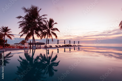 Beautiful poolside and sunset sky. Luxurious tropical beach landscape  deck chairs and loungers and water reflection over the swimming pool. Luxury summer vacation or holiday  hotel resort