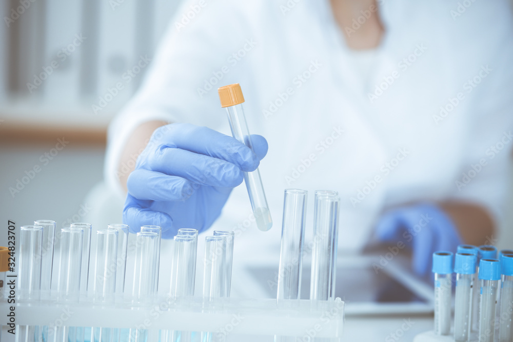 Close-up of professional female scientist in protective eyeglasses making experiment with reagents in laboratory. Medicine and research concept