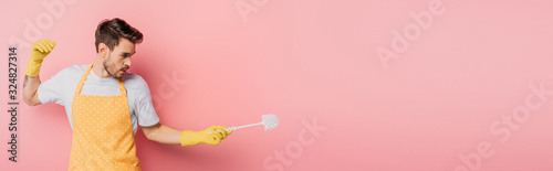 Canvas Print panoramic shot of young man in apron and rubber gloves imitating fencing with pl