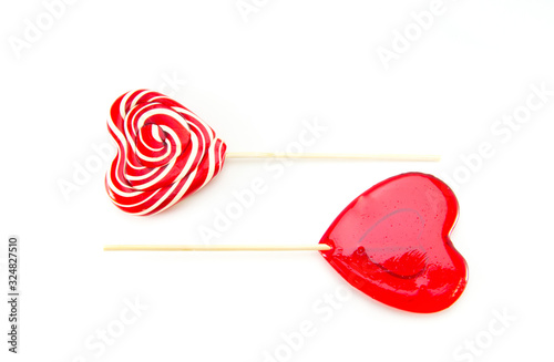Two sweet lollipops in the form of a heart on a wooden stick. One curled, one transparent on a white isolated background arranged horizontally on top of each other. Love and feelings in candy.