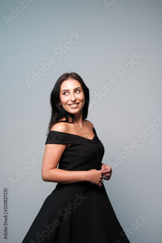 A large portrait of a middle-aged woman (30-35 years old) with dark hair and brown eyes in a black dress on a light background.