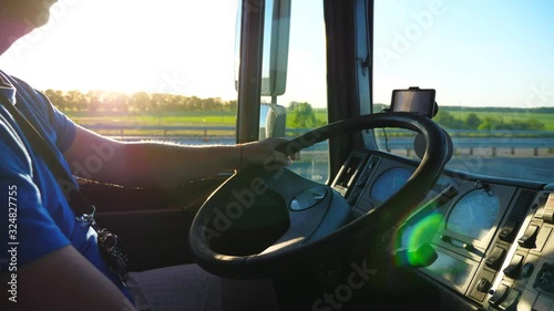 Unrecognizable man sitting behind wheel of his truck and riding through countryside at sunset. Close up steering wheel and dashboard of truck. Beautiful landscape at background. Slow motion Side view