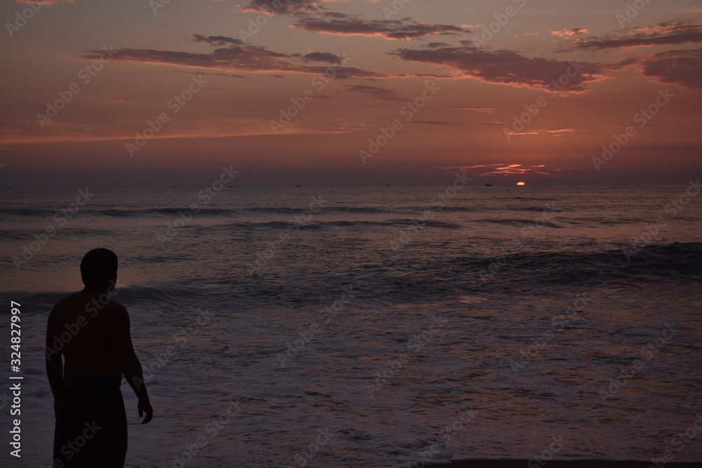 a man standing in a beach to see the sun set in the middle of a ocean