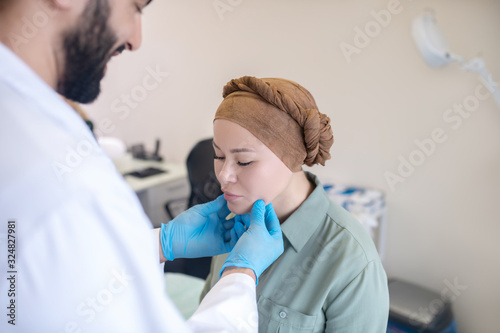 Tall doctor in blue gloves examining his female patient