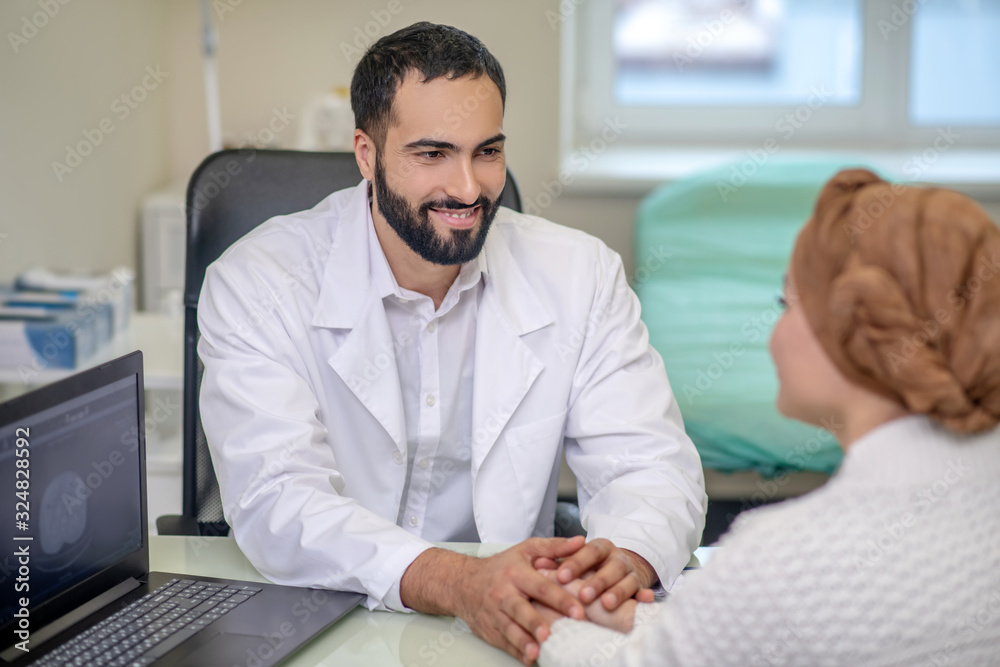 Male doctor holding his female patients hands while talking Male doctor holding his female patients hands while talking