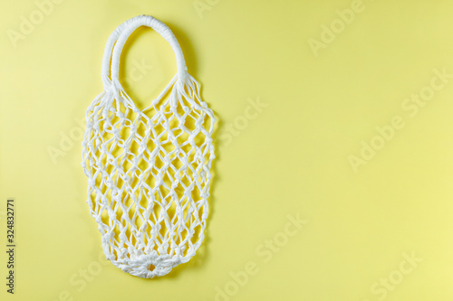 Reusable mesh shopping bag. Empty net bag on yellow background, copy space