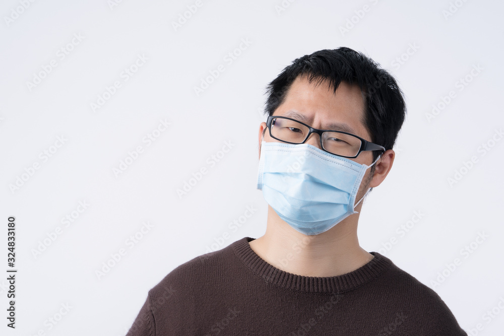 Young Asian man portrait, feeling sick, wearing a surgical blue face mask to prevent infection, air pollution isolated on white background, cut out. Young Asian man portrait, feeling sick, wearing a surgical blue face mask to prevent infection, air pollution isolated on white background, cut out.