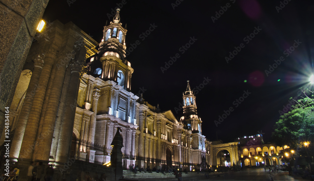 Night photograph of the Basilica Cathedral of the city of Arequipa in southern Peru, the image shows the cathedral illuminated at night with people walking around