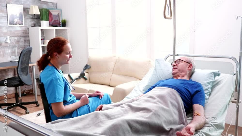 Female doctor talking old man lying in bed in a nursing home Female doctor talking old man lying in bed in a nursing home
