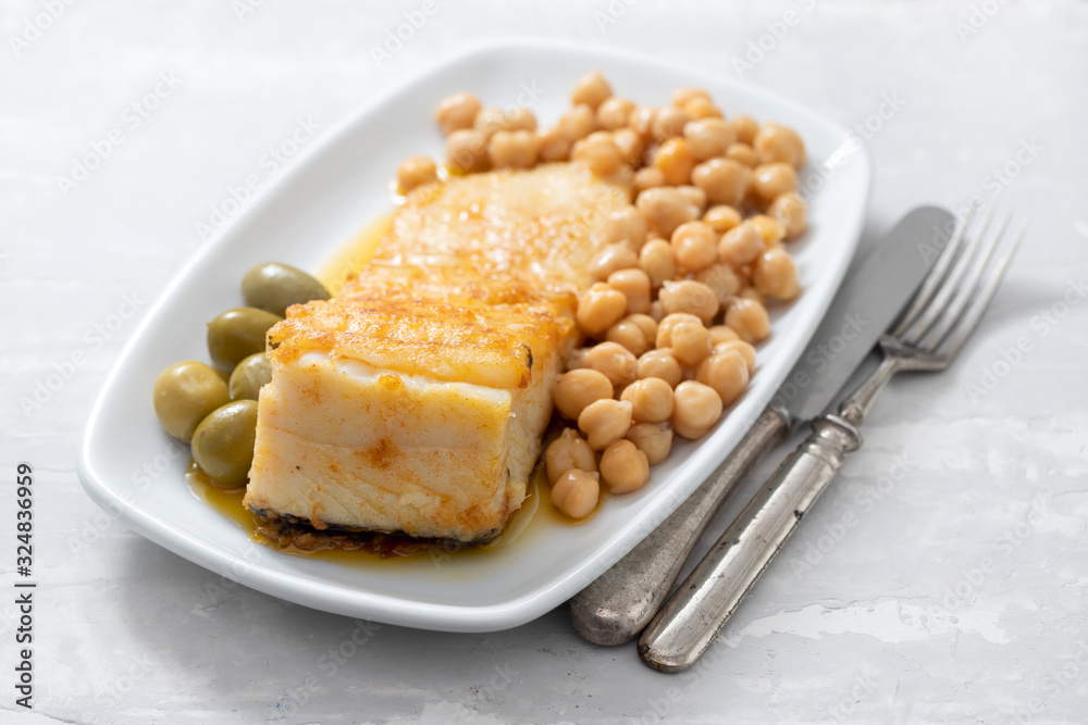 fried cod fish with chick pea and olives on white dish on ceramic background fried cod fish with chick pea and olives on white dish on ceramic background