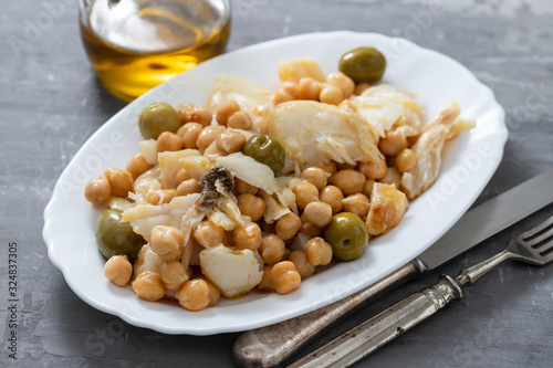 cod fish with chick pea and olives on white dish on ceramic background