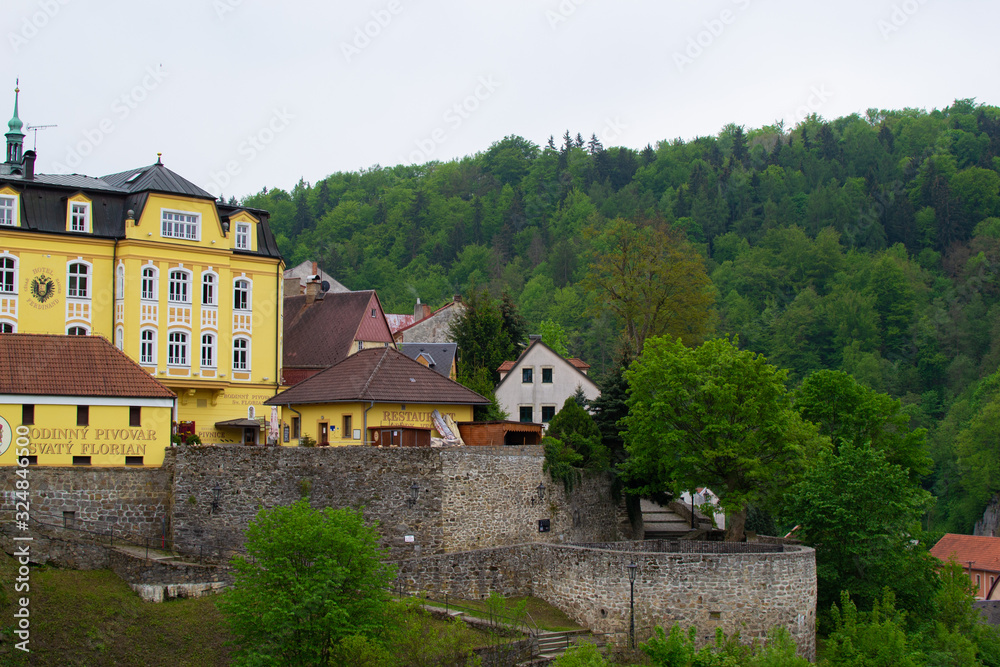 Loket, Czech Republic; 5/20/2019: Yellow building of St. Florian Brewery restaurant, with the stone wall at the foreground and trees at the background
