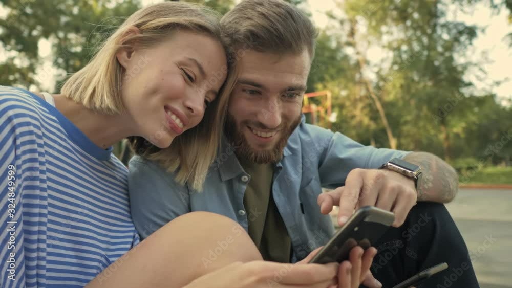 A young beautiful couple man and woman are watching something interesting on the smartphone on the sport area A young beautiful couple man and woman are watching something interesting on the smartphone on the sport area