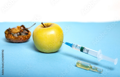 Medicine concept with rotten and fresh yellow apple, ampoule and syringe. Genetically modified fruit on light blue background Copy space