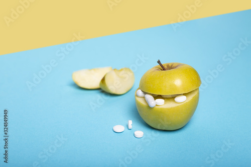 Medicine concept with fresh apple and tablets. Piece of apple. Genetically modified fruit on blue and yellow background