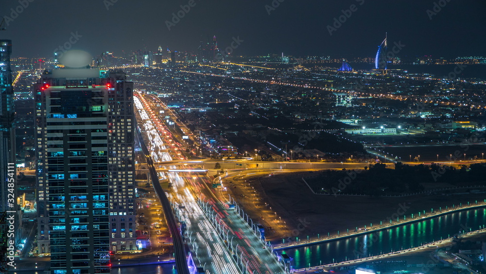 Obraz premium Dubai business bay towers illuminated at night timelapse. Rooftop view of some skyscrapers and new towers under construction.