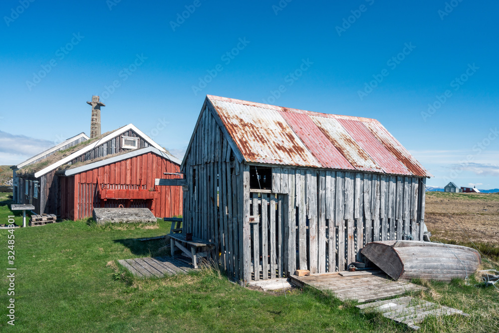 Old and weathered building on Flatey in Iceland. Factory pipe in the background. Blue sky during springtime Old and weathered building on Flatey in Iceland. Factory pipe in the background. Blue sky during springtime
