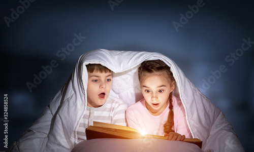 Children reading scary stories in bed