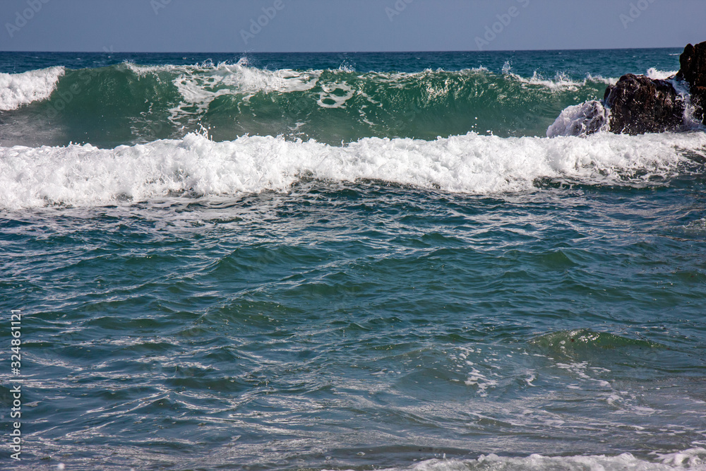 The frothy waves of the sea break on the rocks and on the beach.