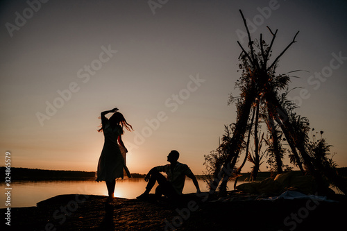 Young couple is embracing in the water on Sunset. Two silhouettes against the sun. Romantic love story. Wigwam on the stone. photo