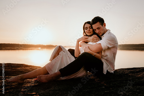 Young couple embracing and kissing on Sunset coast. Romantic love story. Brunette girl in a light dress.