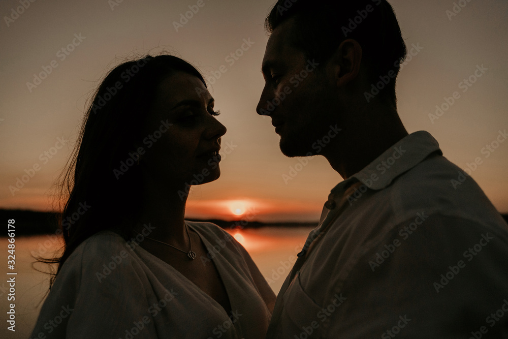 Young couple is embracing on the sunset coast. Two silhouettes against the sun. Romantic love story. Young couple is embracing on the sunset coast. Two silhouettes against the sun. Romantic love story.