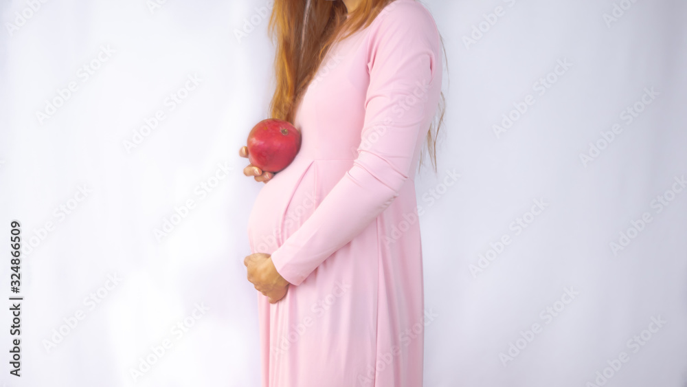 A close up photo of a pregnant young woman holding a mango next to her belly showing the size of the baby in a beautiful dress. Photos of fetal growth at 19 week pregnancy. Healthy pregnancy diet. A close up photo of a pregnant young woman holding a mango next to her belly showing the size of the baby in a beautiful dress. Photos of fetal growth at 19 week pregnancy. Healthy pregnancy diet.