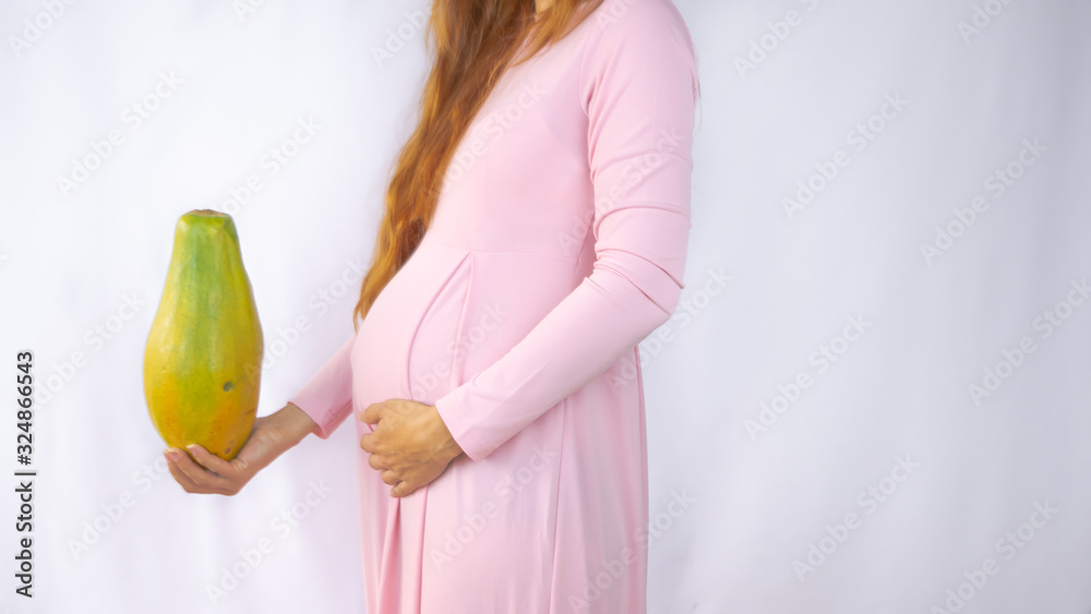 A close up photo of a pregnant young woman holding a papaya next to her