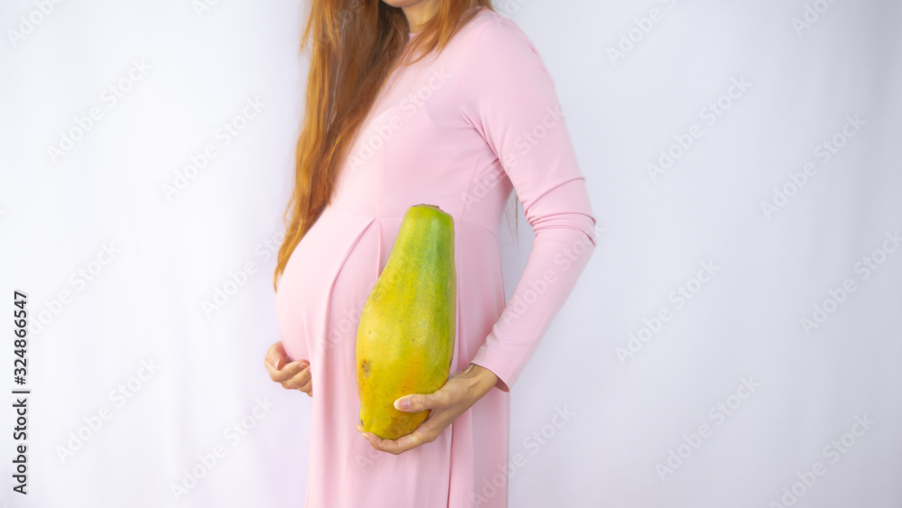 A close up photo of a pregnant young woman holding a papaya next to her