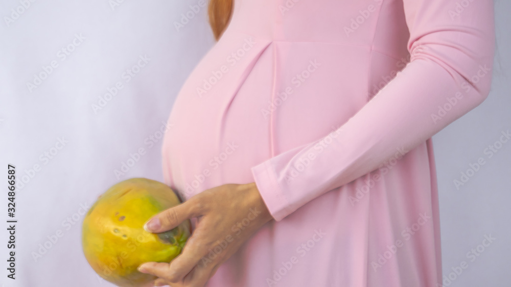 A close up photo of a pregnant young woman holding a papaya next to her
