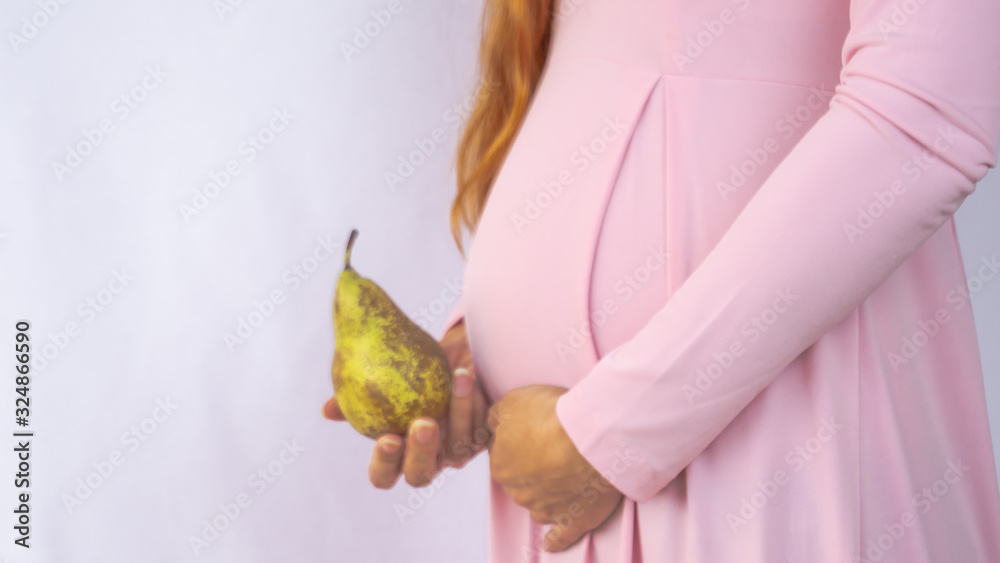A close up photo of a pregnant young woman holding a pear next to her