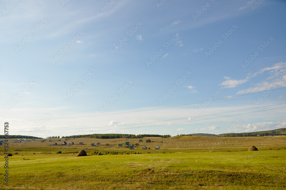 Fototapeta premium Light white clouds in the warm summer sky over village with small houses far away in the fields. Travelling. People living