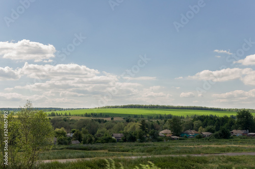 Light white clouds in the warm summer sky over village with small houses far away in the fields. Travelling. People living 