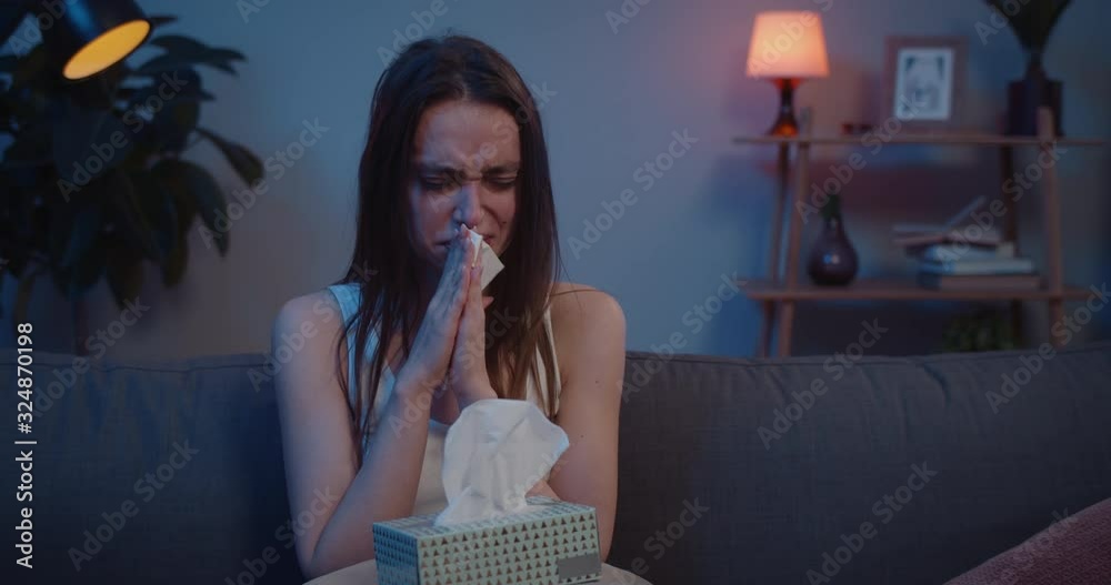 Close up of unhappy woman sitting on sofa using paper tissues, crumpling them and throwing away. Young crying girl with box of handierchief blowing nose and thinking. Emotional breakdown.