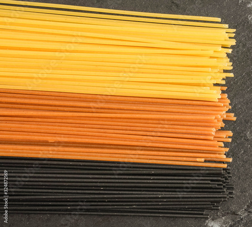 Spaghetti in three colors on a black basalt background