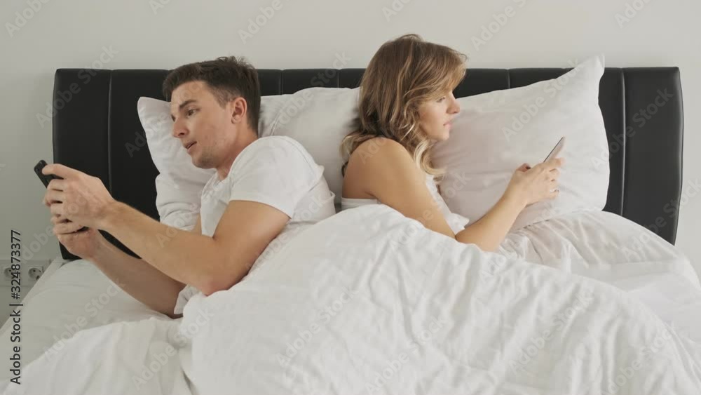 A focused couple are lying in bed back to back using cellphones top view A focused couple are lying in bed back to back using cellphones top view