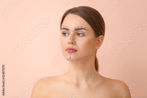 Young woman with marks on her face against color background. Concept of plastic surgery