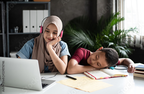 The beaytiful lady put headphone on her head and using laptop for doing work,beside sleeping brother,at home