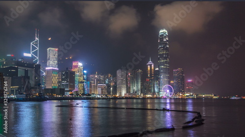 Hong Kong city skyline at night over Victoria Harbor with cloudy sky and urban skyscrapers timelapse hyperlapse.