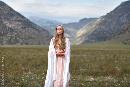 A girl walks through the meadow against the backdrop of the mountains. Prayer.