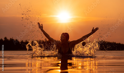 silhouette of woman splashing water in infinity pool at sunset